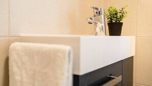 Een badkamer met een witte wastafel, een potplant en een handdoek op een rek.