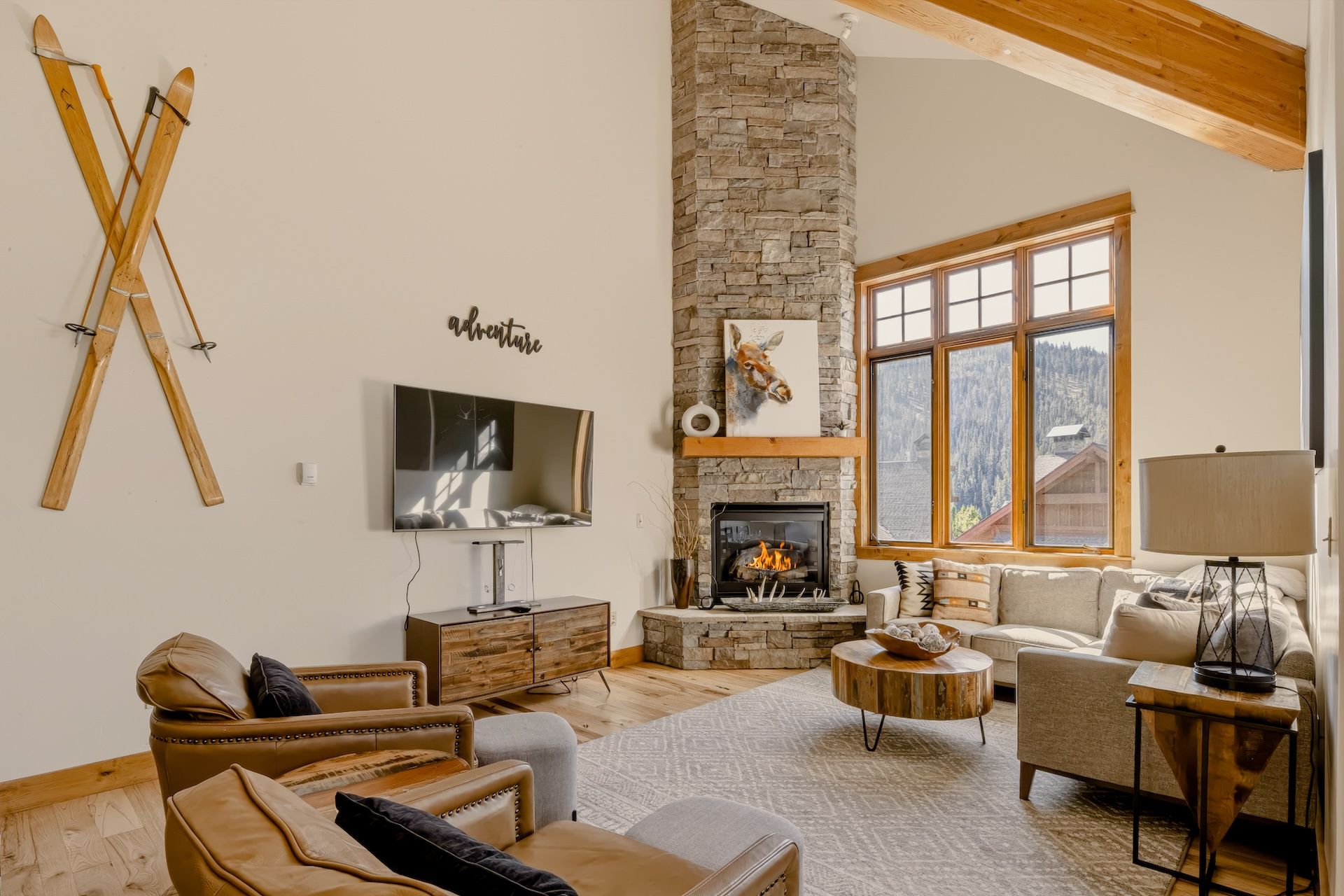 Relax in your spacious living room featuring soaring vaulted ceilings, a cozy stone fireplace, and warm mountain light streaming through floor-to-ceiling windows.