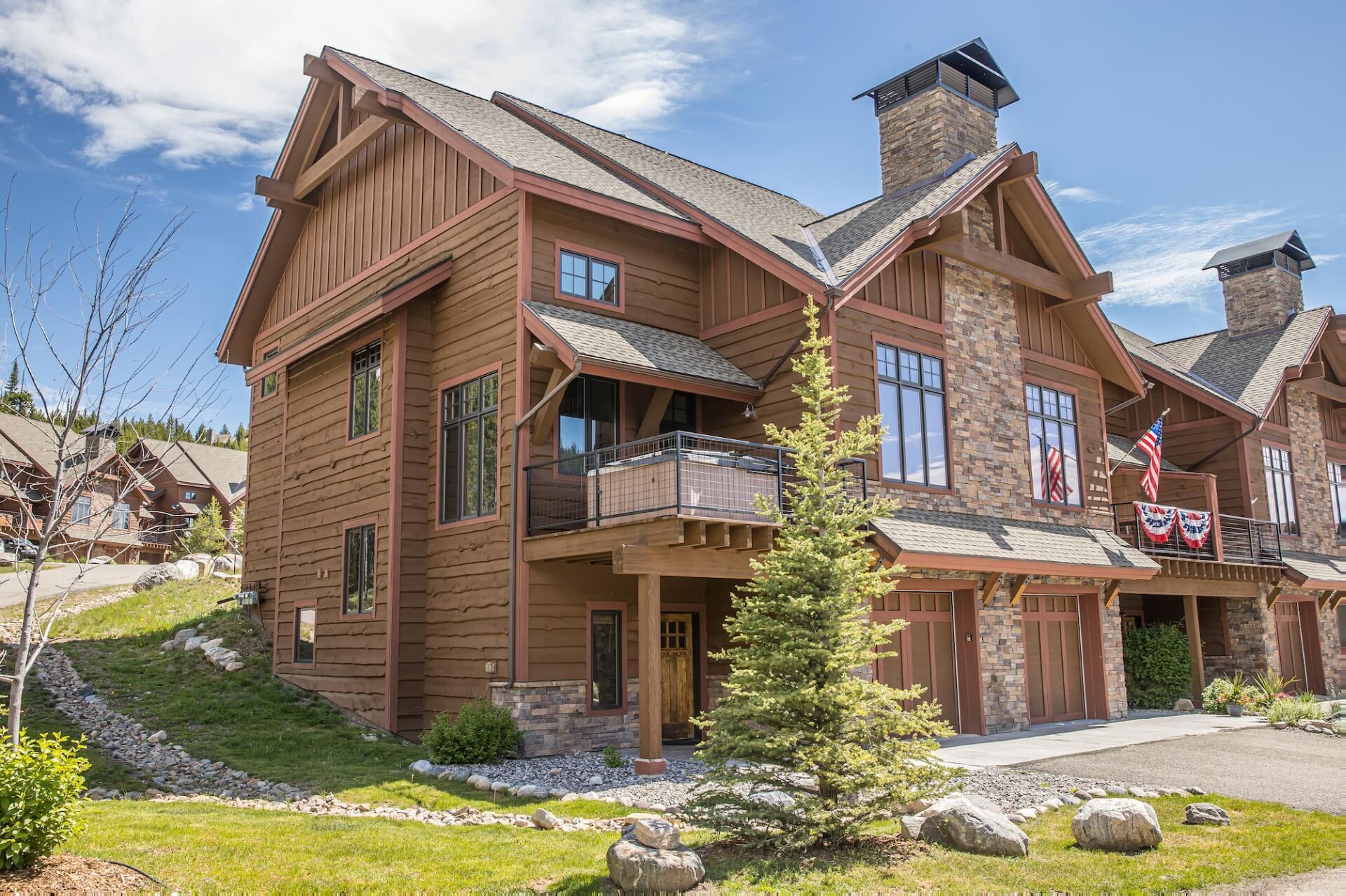 Un bâtiment de style chalet en bois, doté de plusieurs balcons, de cheminées en pierre et d’une pelouse bien entretenue.