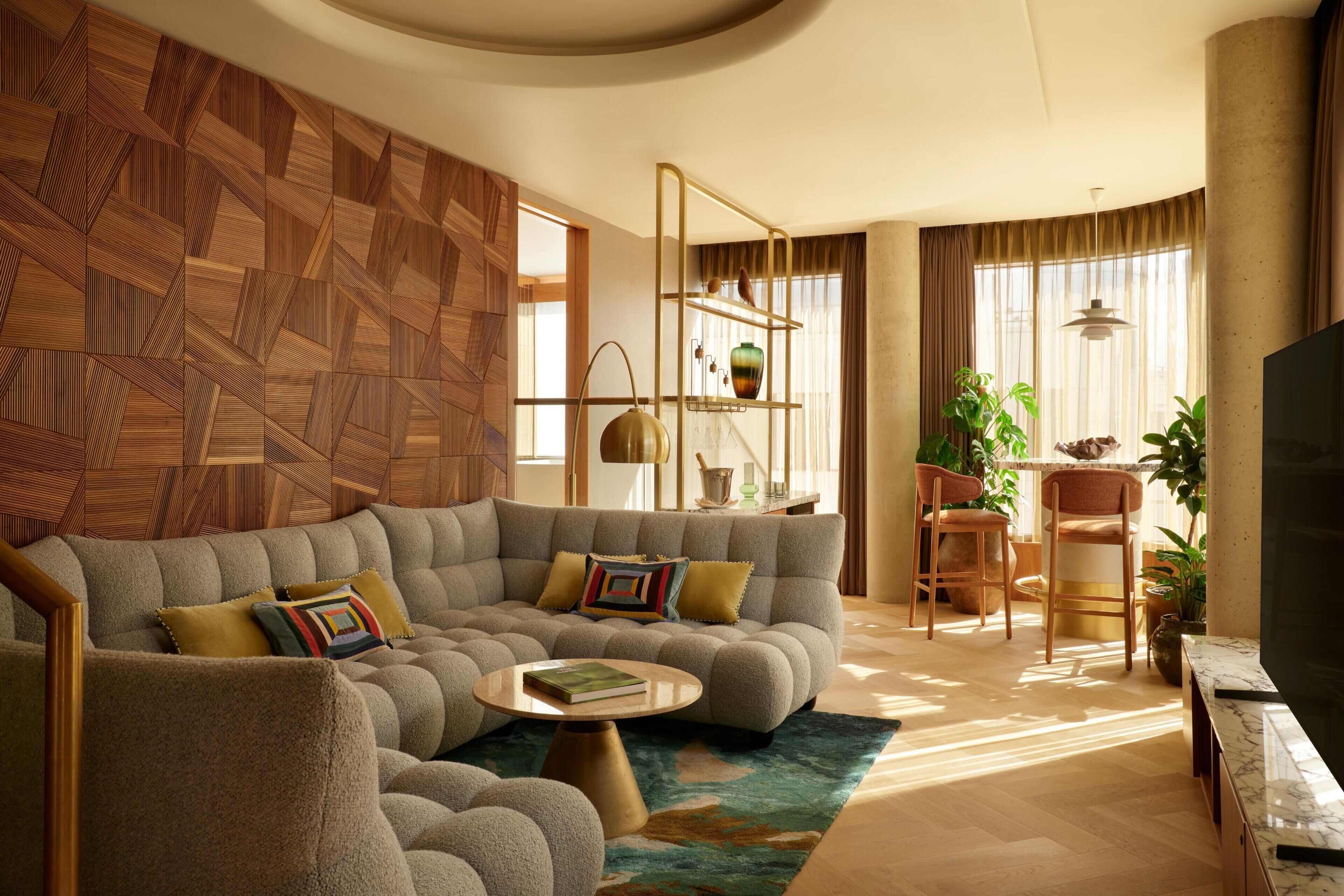Una sala de estar moderna con un sofá modular, una mesa de centro y un televisor. Hay plantas, una estantería y un comedor con sillas.