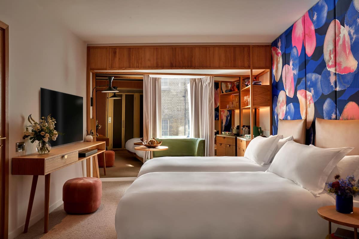 A hotel room with a large bed, a desk with a flat-screen TV, a small table, and a wardrobe.