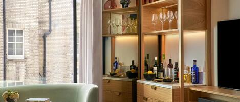 A modern living room with a television, a seating area with a table and books, and a kitchen area with wine bottles and glasses.