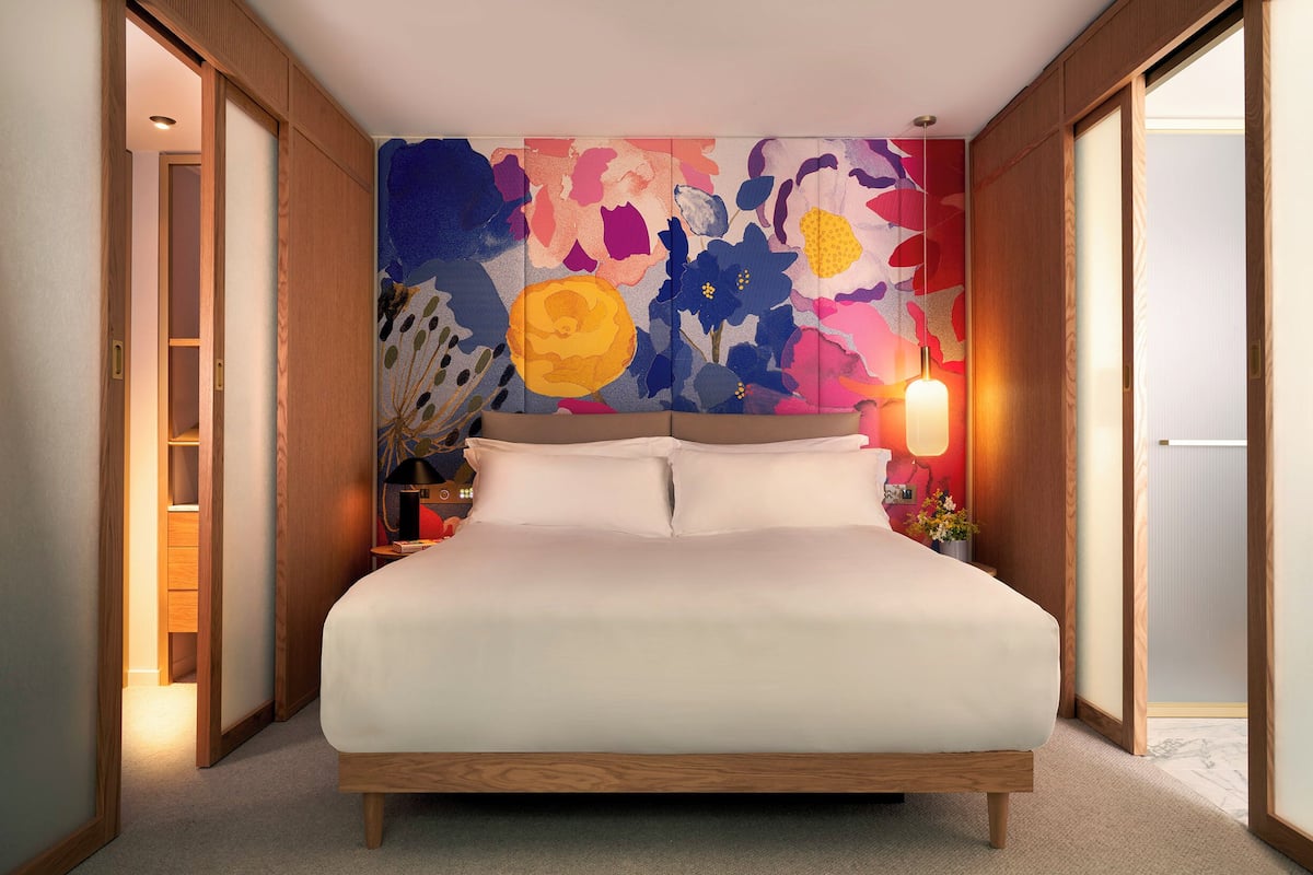 A bedroom with a large bed, wooden headboard, and a colorful floral wall mural.