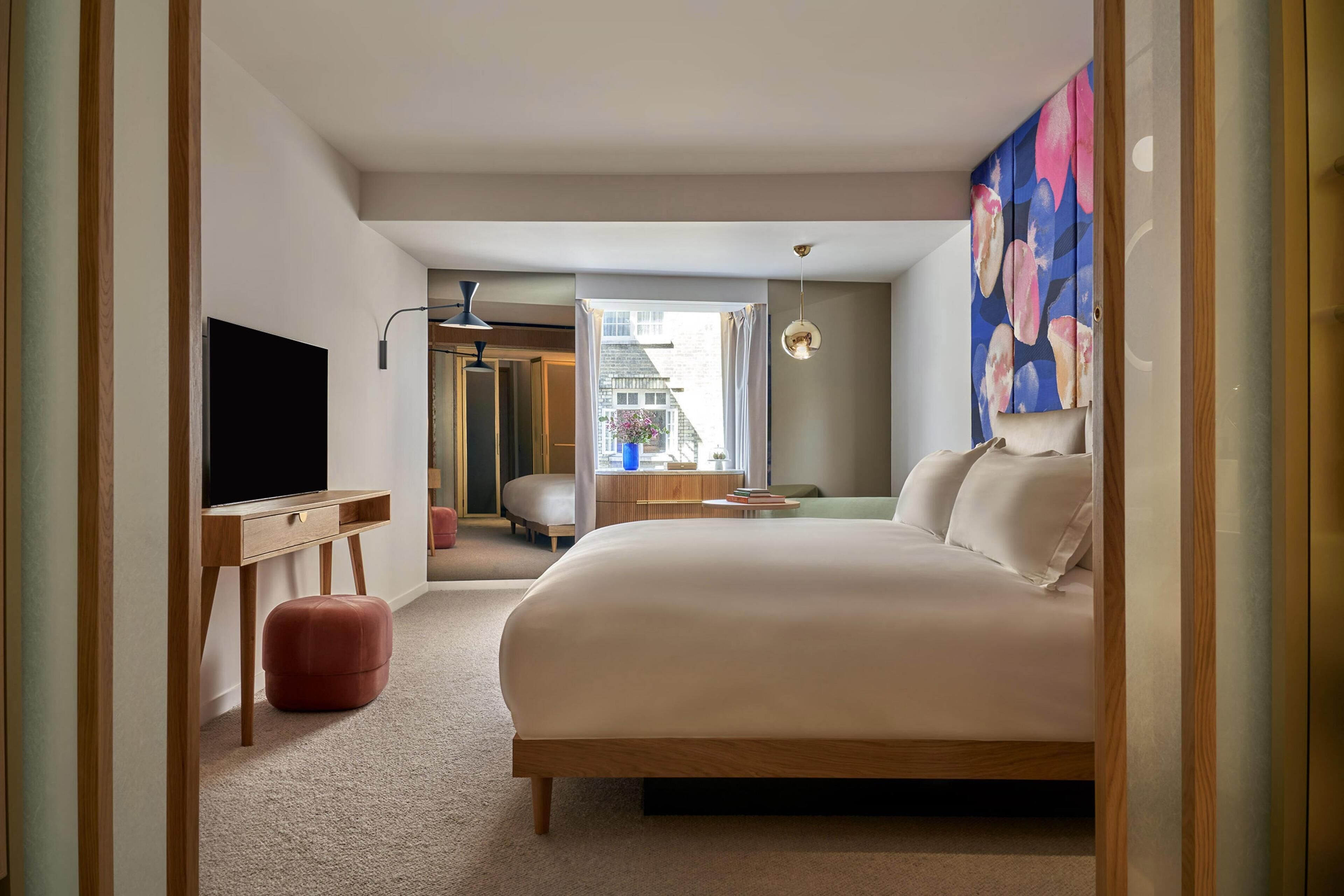 Une chambre d’hôtel moderne dotée d’un grand lit, d’un bureau avec un téléviseur à écran plat, d’un petit coin salon et offrant une vue sur la ville.