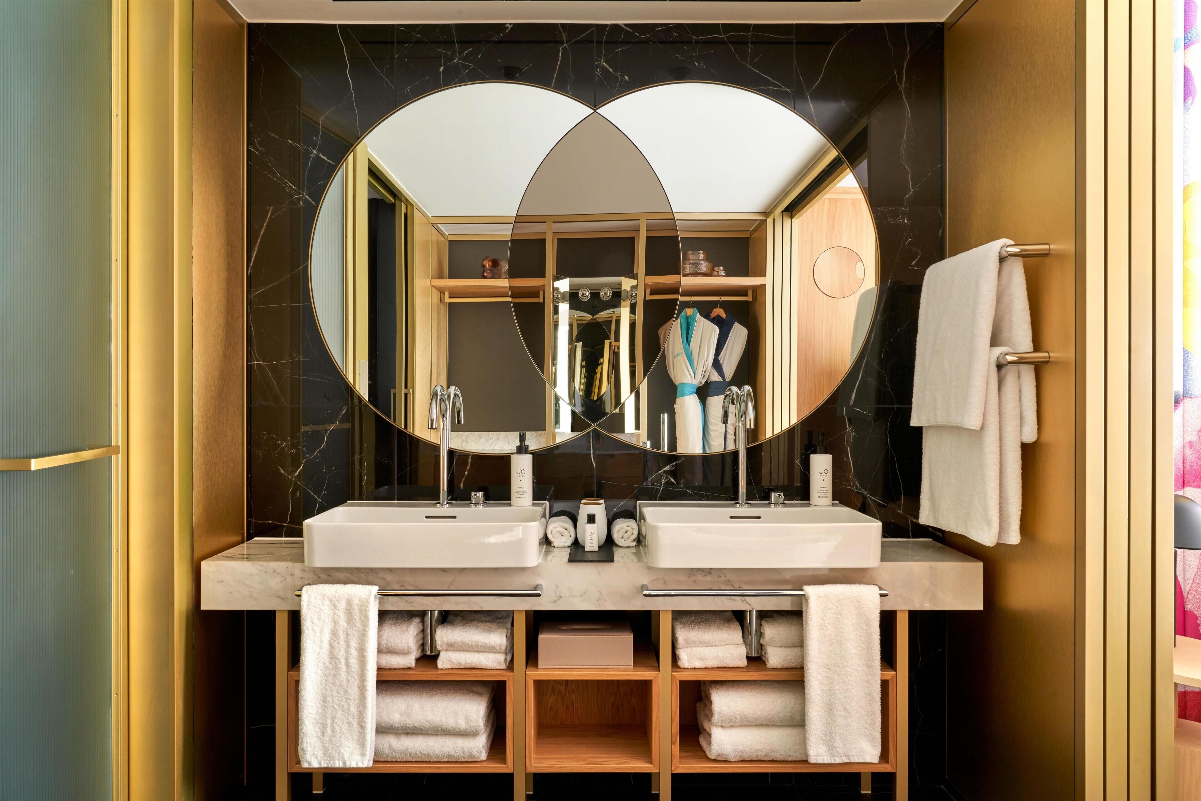 A modern bathroom with two sinks, a large mirror, and a vanity with shelves for towels.