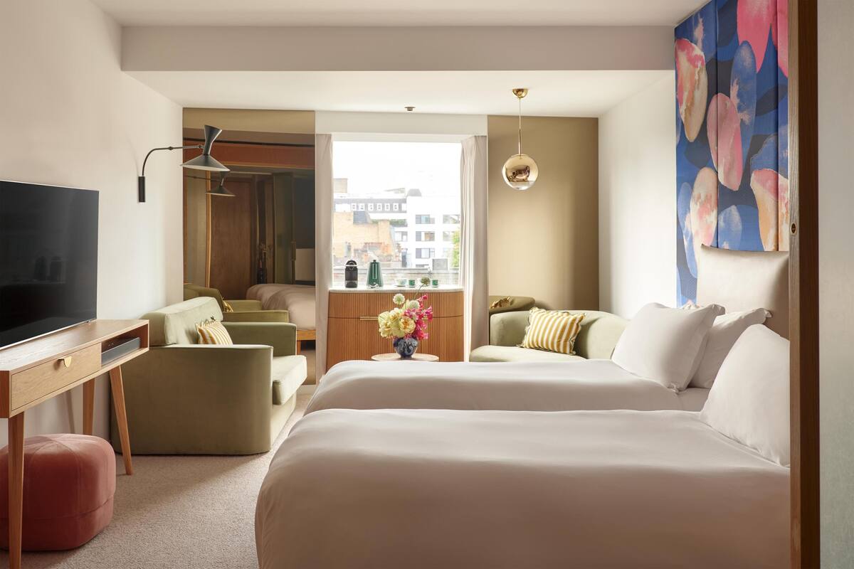 A hotel room with a large bed, a desk with a TV, a sofa, and a view of buildings outside.