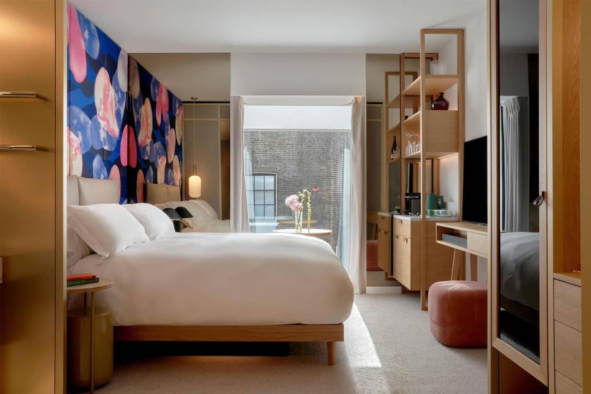 A modern hotel room with a large bed, a desk, a television, and a view of the outside.