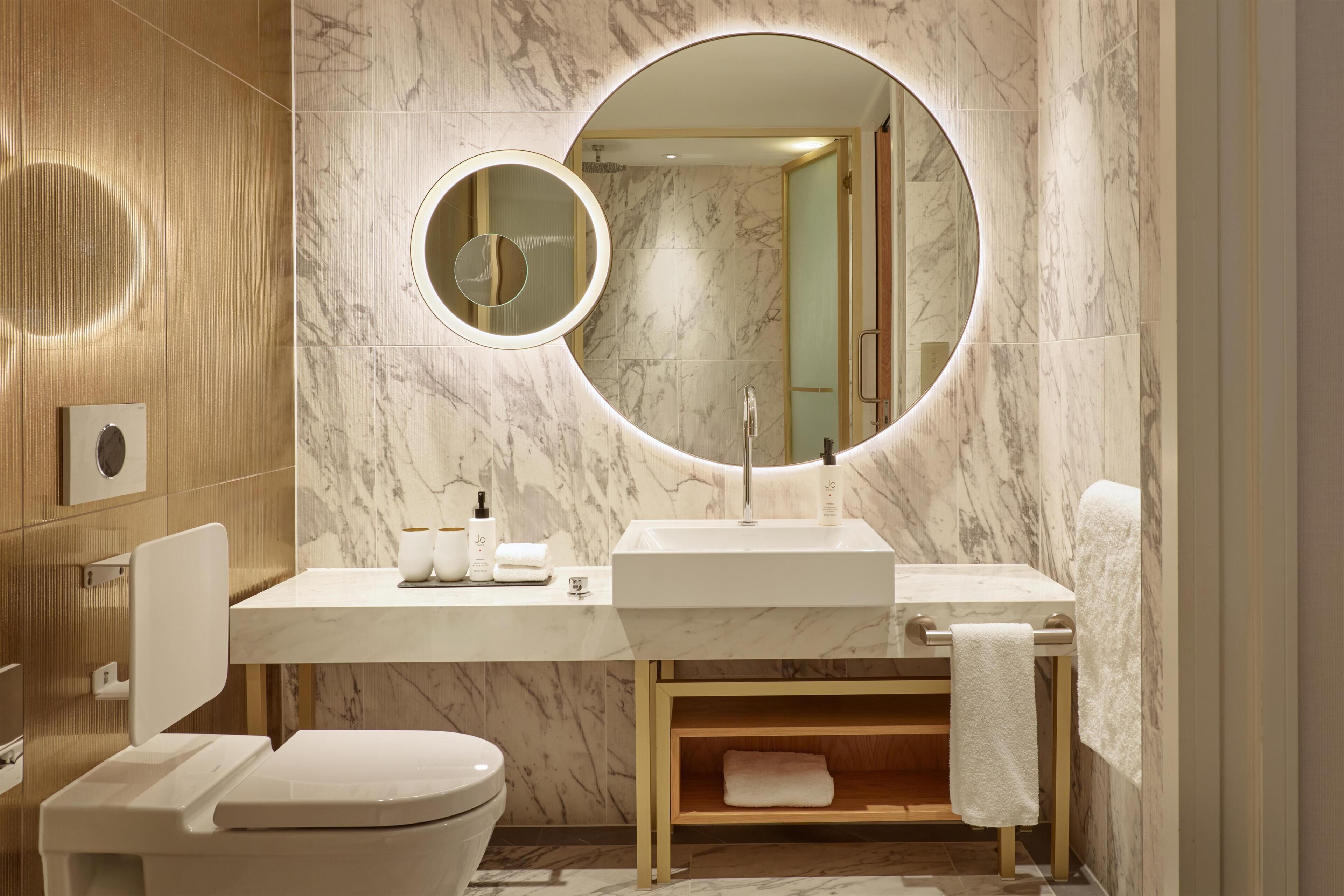 A modern bathroom with a white sink, a toilet, a mirror, and a towel rack.