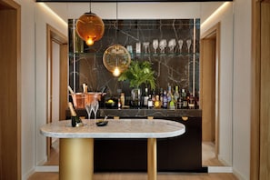 A bar area with a marble countertop, a bottle of champagne, and a glass. There are shelves with bottles and glasses in the background. - The BoTree London, Curio Collection by Hilton (London)