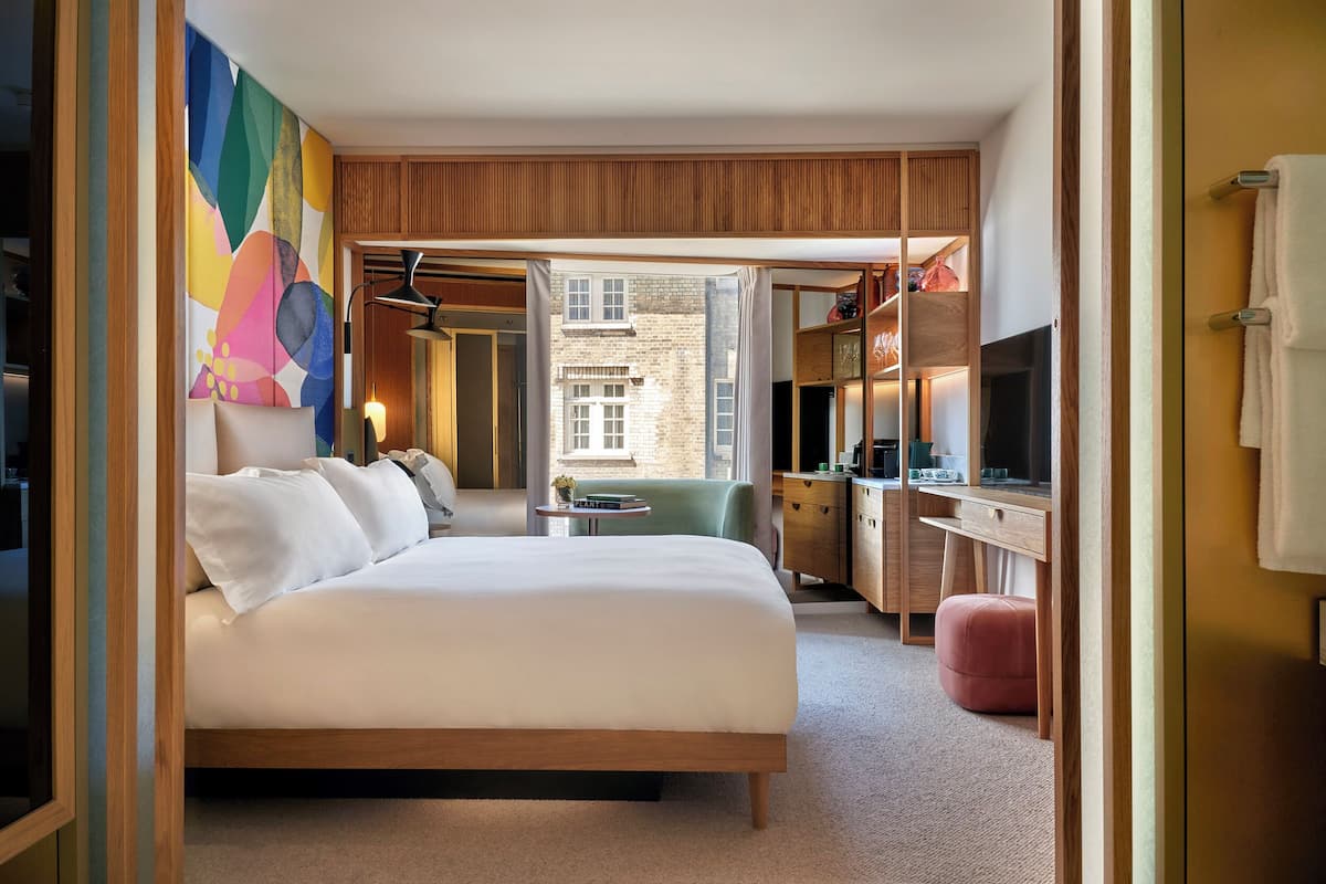 A modern hotel room with a large bed, a desk, a television, and a view of the city.
