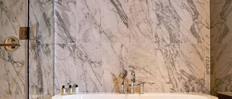 Un baño moderno con una bañera independiente, cabina de ducha con mampara de vidrio y suelo de mármol.