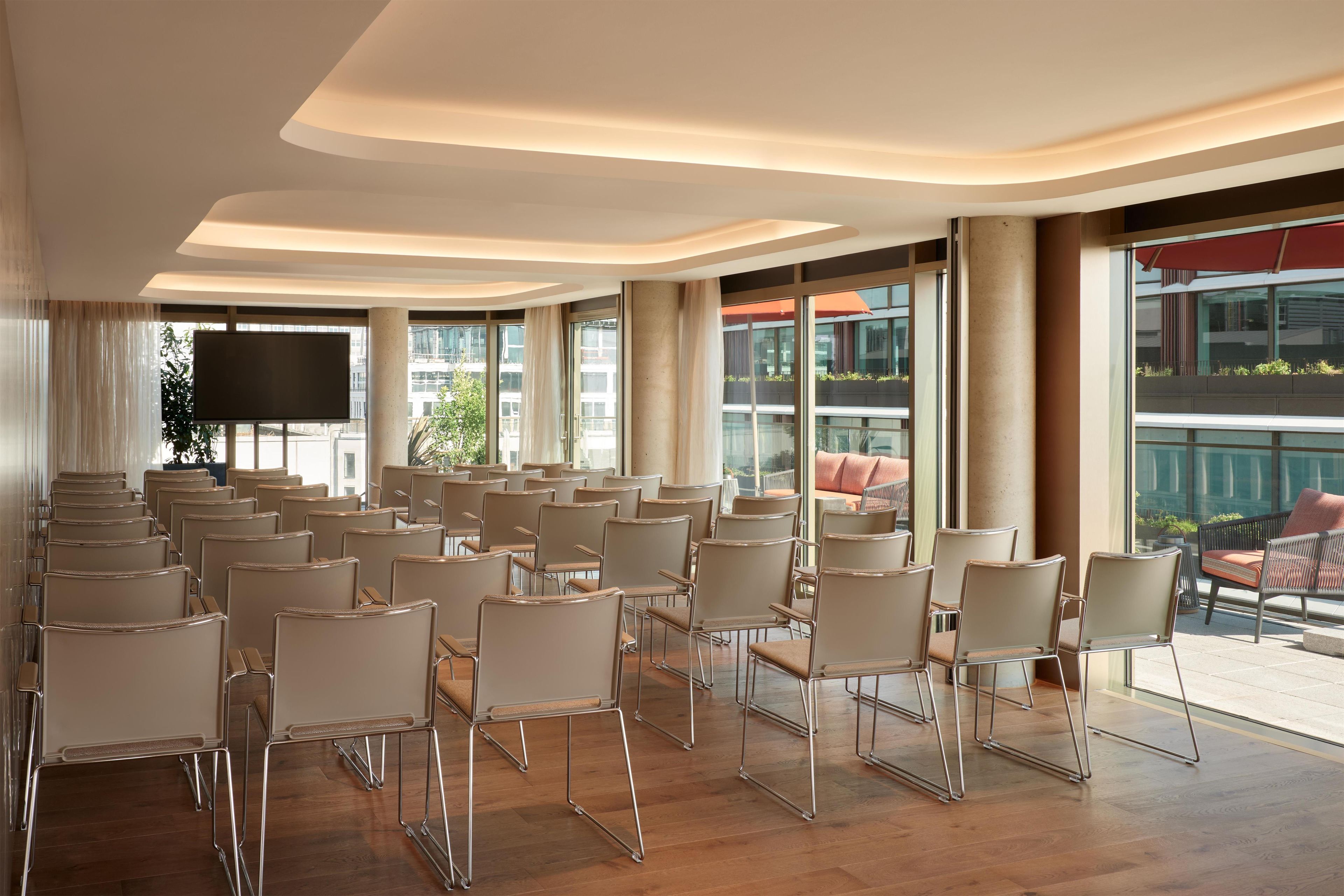 A conference room with rows of chairs, a large screen, and large windows offering views of the city.