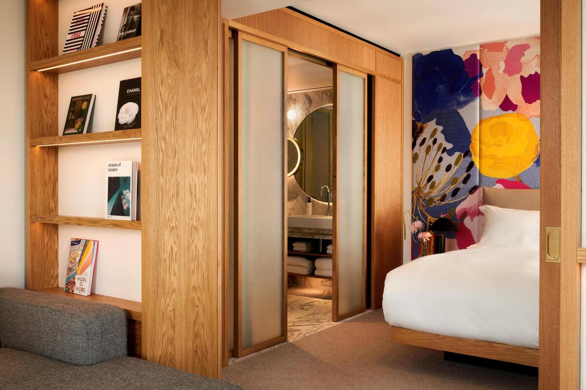 A bedroom with a bed, a wooden bookshelf, a sliding door, and a colorful abstract painting.