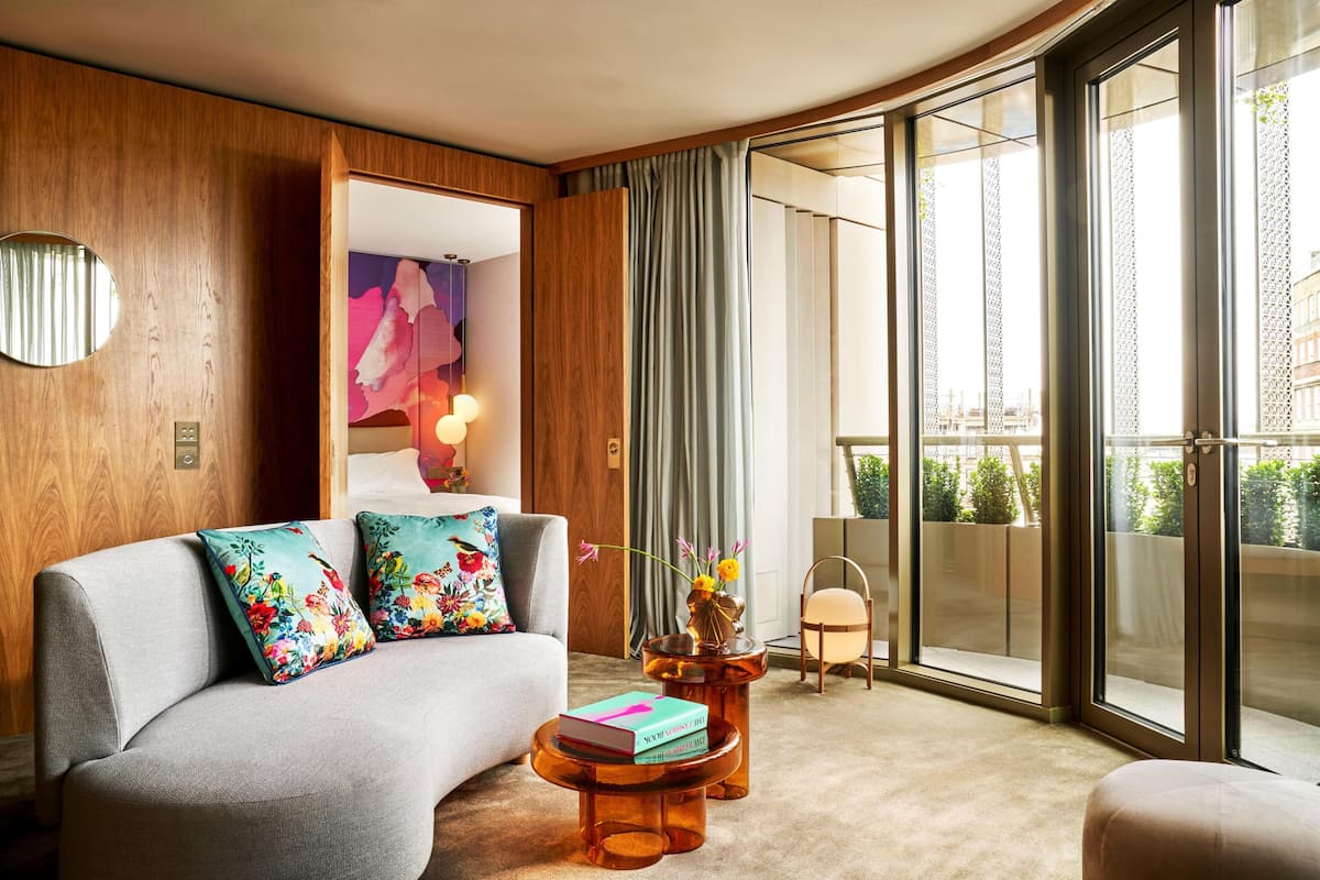 A modern living room with a grey sofa, floral cushions, a round coffee table, and a view of the outdoors through large sliding glass doors.