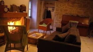 A cozy living room with a fireplace, a sofa, a chair, and a small table. - Maisons de Montagne Typiques 2 (Frasseto)
