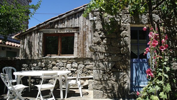 A rustic stone building with a wooden window and a blue door. There is a white table and four chairs outside. - Maisons de Montagne Typiques 2 (Frasseto)