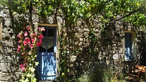 A stone building with a blue door and window, surrounded by greenery and a small garden area. - Maisons de Montagne Typiques 2 (Frasseto)