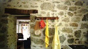 A rustic kitchen with stone walls, a wooden beam ceiling, and a hanging rack with kitchen towels. - Maisons de Montagne Typiques 2 (Frasseto)