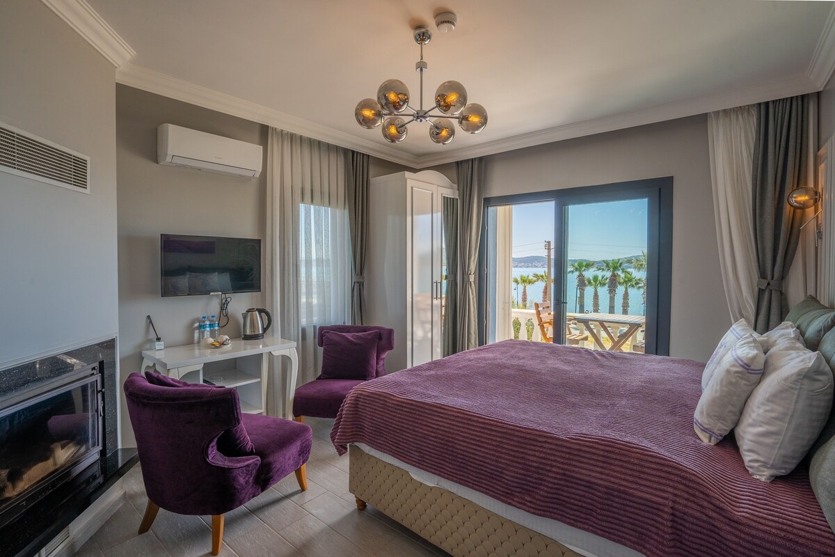 A hotel room with a large bed, a desk, a chair, a TV, and a fireplace.