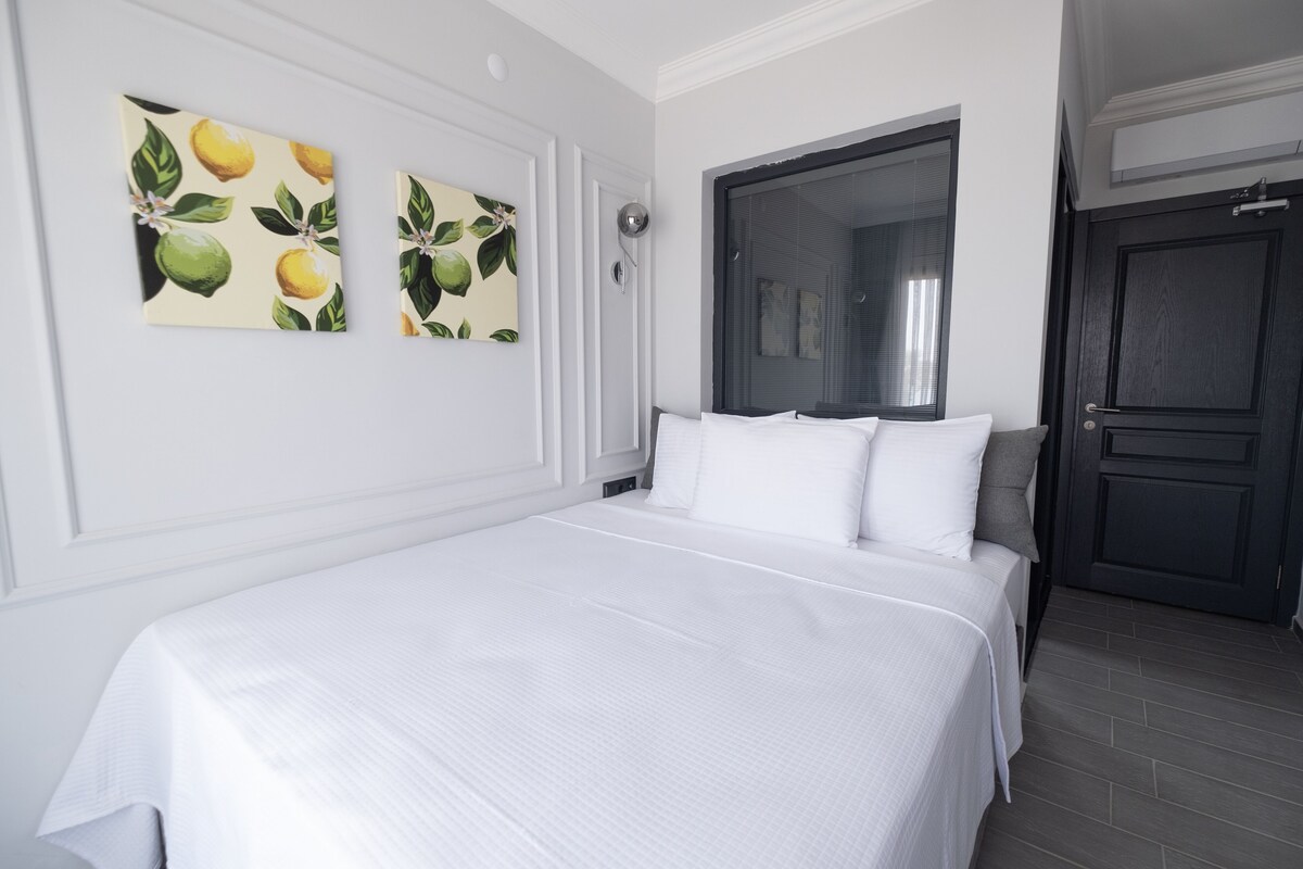 A hotel room with a large bed, white bedding, and two wall-mounted paintings of lemons and leaves.