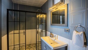Un baño moderno con ducha envuelta en vidrio, un lavamanos blanco y una toalla colgada en un perchero metálico.