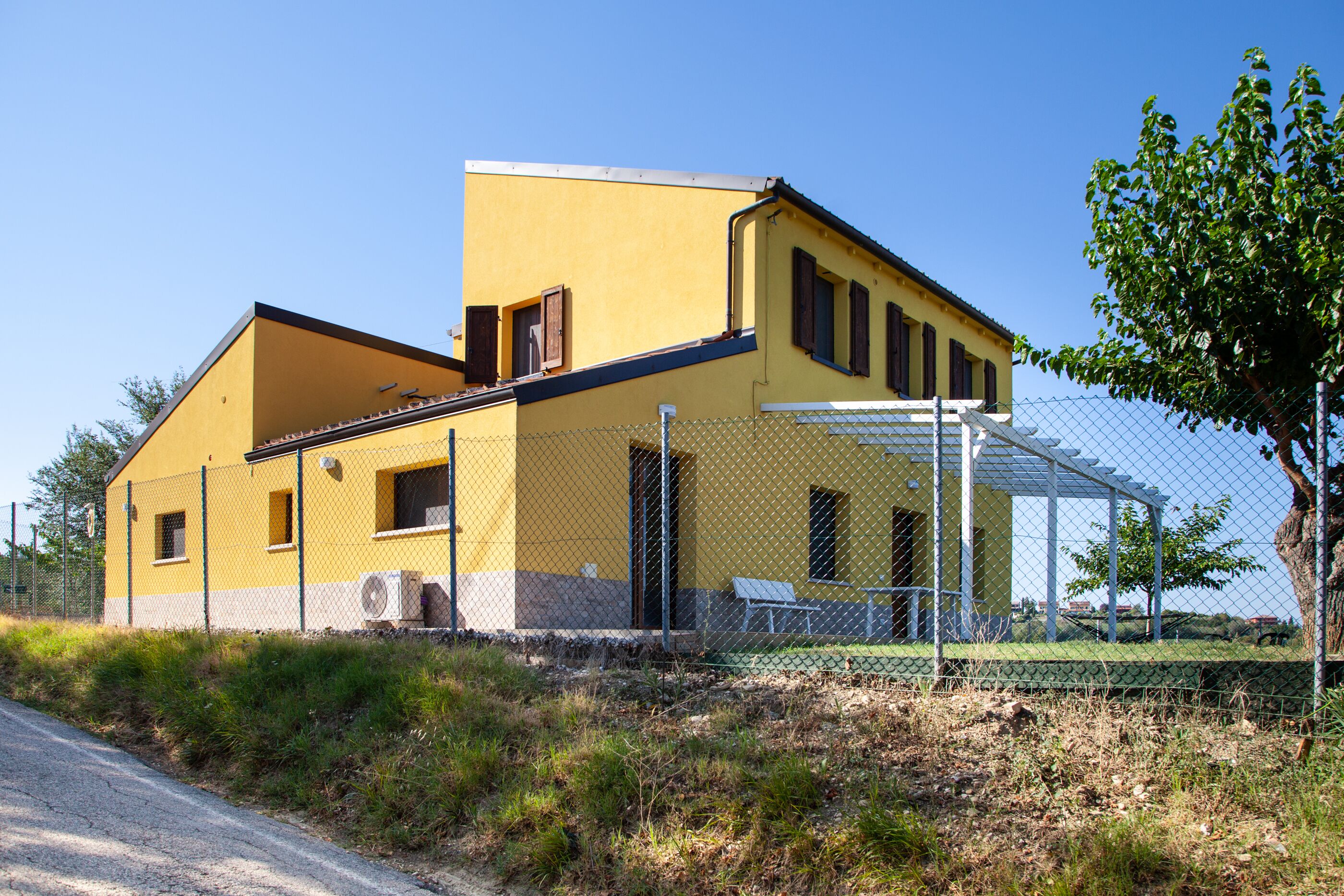 A yellow building with a fenced outdoor area and a pergola.