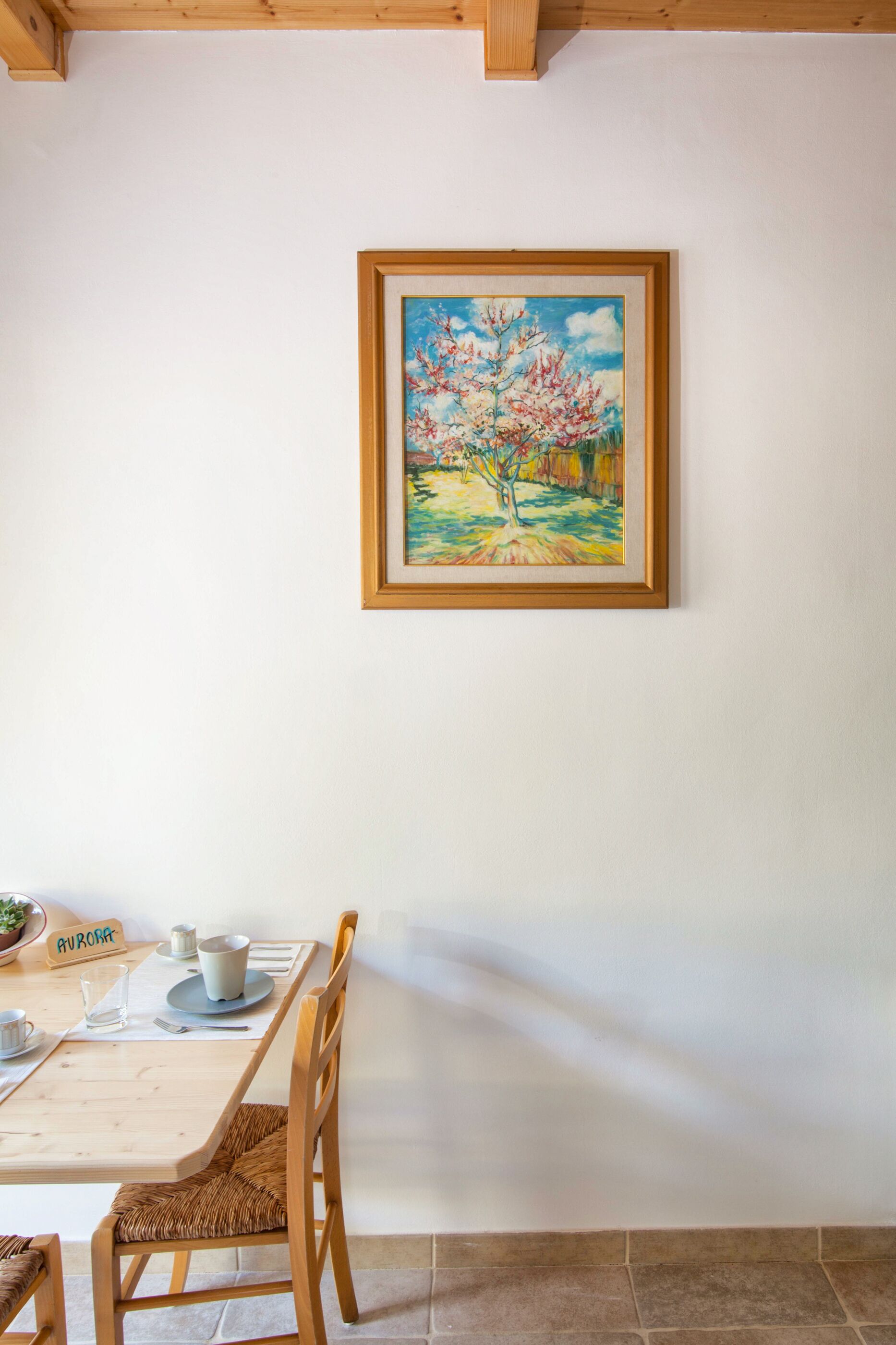A dining area with a wooden table, chairs, and a framed painting of a tree.