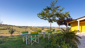 Een terras met tafels en stoelen, omringd door groen en een uitzicht op het landschap.