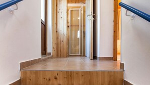 Een houten trap met een leuning, die leidt naar een kamer met een houten plafond en een deur.