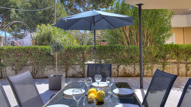 An outdoor dining area with a table set for four, surrounded by chairs, under a large umbrella. - Playamar by Rentallorca (Puerto de Alcudia)