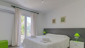 A bedroom with a bed, bedside tables, a green bench, and a window with curtains. - Playamar by Rentallorca (Puerto de Alcudia)
