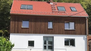 Una casa a due piani con tetto in tegole rosse, rivestimento in legno e fondamenta in pietra.