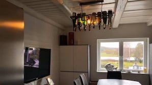 Zona pranzo con tavolo e sedie, televisore su supporto e finestra con vista sull'esterno.