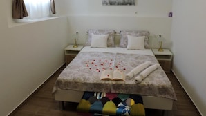 Een slaapkamer met een bed, twee nachtkastjes, een bankje, een schilderij aan de muur en een raam met gordijnen.