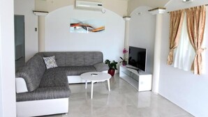 Een moderne woonkamer met een grijze modulaire bank, een witte salontafel, een flatscreen televisie en een potplant.