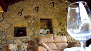 A stone fireplace with a hanging light fixture, a cushioned seating area, and a wine glass on a table. - A beira da cortella (Melón)