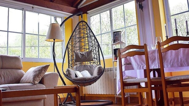 A cozy room with a wooden ceiling, a hanging chair, a sofa, and a dining table with chairs. - A beira da cortella (Melón)
