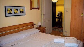A neatly made bed with white linens, a bedside lamp, and a framed picture of flowers on the wall. - A beira da cortella (Melón)