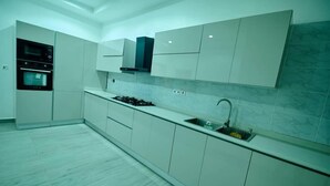 Uma cozinha moderna com armários brancos, forno embutido, fogão a gás e pia de aço inoxidável.