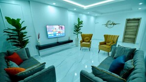 Uma sala de estar moderna com uma televisão de tela plana, duas poltronas, um sofá e uma planta grande.