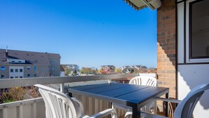 A balcony with a table and chairs, overlooking a residential area with various buildings. - Muschelbank Wohnung 59 (Büsum)