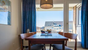 A dining area with a wooden table and chairs, a hanging light fixture, and a view of buildings through a glass door. - Muschelbank Wohnung 59 (Büsum)