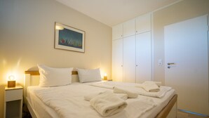 A neatly made bed with white linens and towels, a bedside lamp, and a painting on the wall. - Muschelbank Wohnung 59 (Büsum)