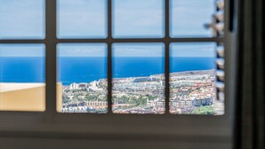 Une vue à travers une fenêtre à carreaux, donnant sur un paysage urbain côtier avec des bâtiments et la mer.