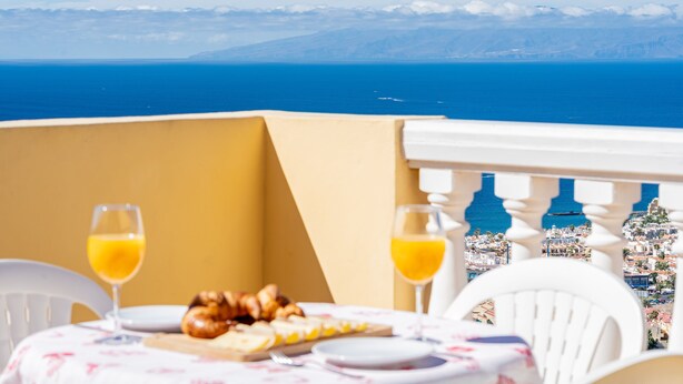 Une table dressée avec des aliments et des boissons pour le petit-déjeuner, offrant une vue imprenable sur une ville côtière, la mer et les montagnes lointaines.
