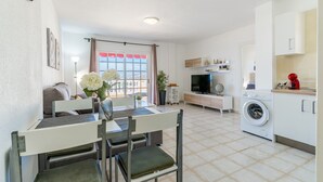 Un espace de vie compact comprenant un coin repas, un téléviseur, un lave-linge et un coin cuisine.