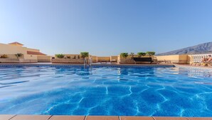 Une piscine d’un bleu éclatant, avec une terrasse carrelée au premier plan, entourée de petits murets et de plantes en pot.