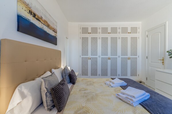 A bedroom with a large bed, a headboard, a painting on the wall, and a set of louvered doors.