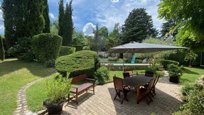 A patio area with a table and chairs, surrounded by well-maintained hedges and a pool in the background. - Villa with pool and garden - 30' from Lyon (Saint-Just-Chaleyssin)