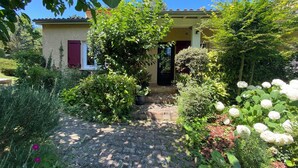 A house with a paved driveway leading to a front door, surrounded by lush greenery and flowering plants. - Villa with pool and garden - 30' from Lyon (Saint-Just-Chaleyssin)